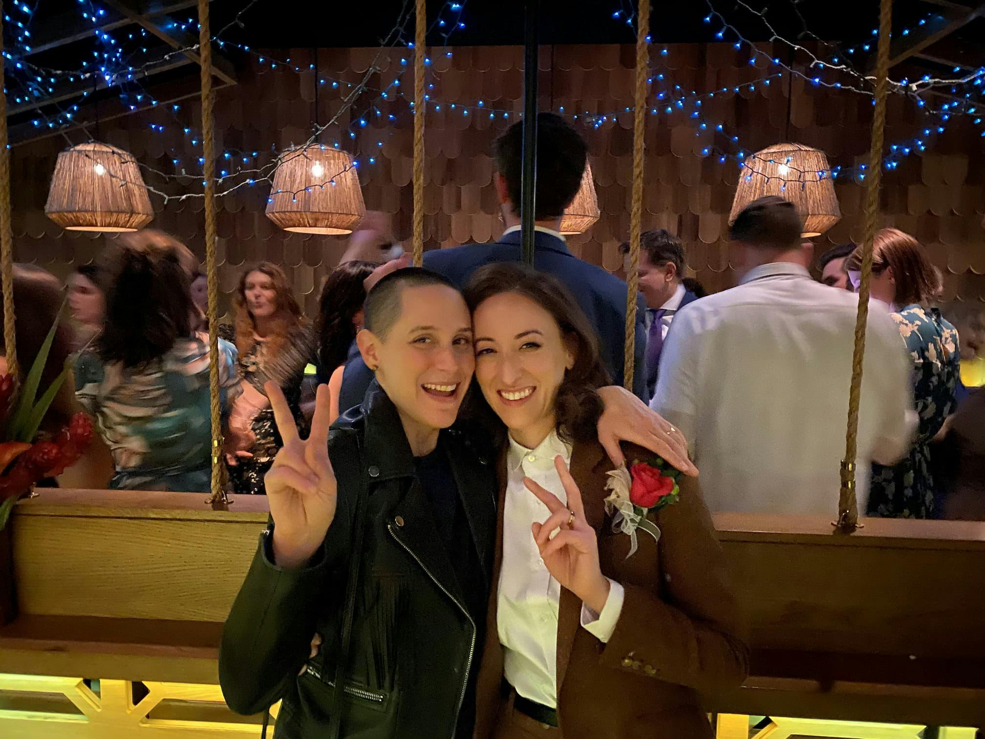 Carla and Alessia as guests at Véro and Geoff's wedding, smiling beside the dance floor and flashing the peace sign